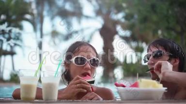 快乐的年轻夫妇戴着太阳镜，度假时在游泳池里吃<strong>水果</strong>。 1920x1080